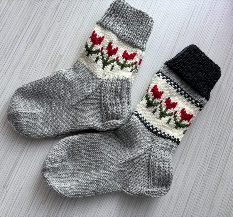 May include: Two pairs of gray knitted socks with white and red tulip designs. The socks have a black cuff on one pair.