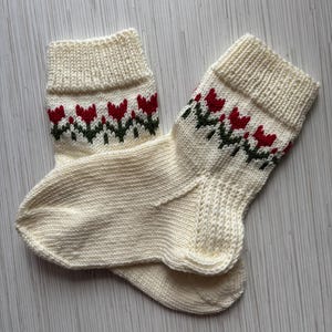 May include: A pair of white knitted socks with a red and green floral pattern.