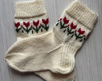 May include: A pair of white knitted socks with a red and green floral pattern.