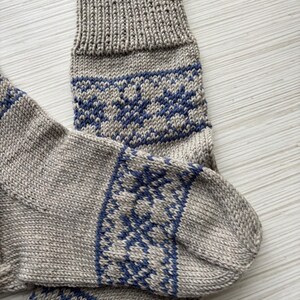 May include: A pair of knitted socks with a grey base and blue snowflake pattern. The socks are folded and the top of the sock is visible.