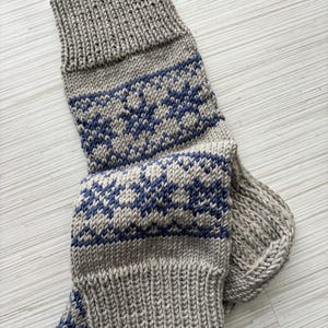 May include: A pair of knitted socks with a grey and blue geometric pattern. The socks are folded and the top of the sock is visible.