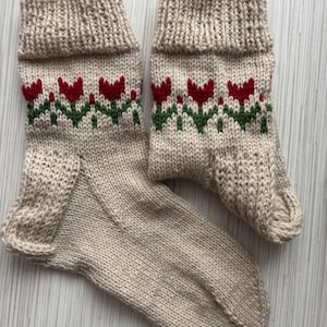 May include: A pair of beige knitted socks with a red and green floral pattern. The socks are made of a soft, comfortable material and have a ribbed cuff.