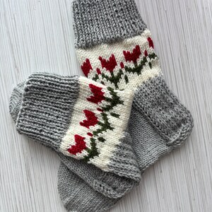 May include: A pair of gray knitted socks with a white and red floral pattern. The socks are folded together and have a ribbed texture.