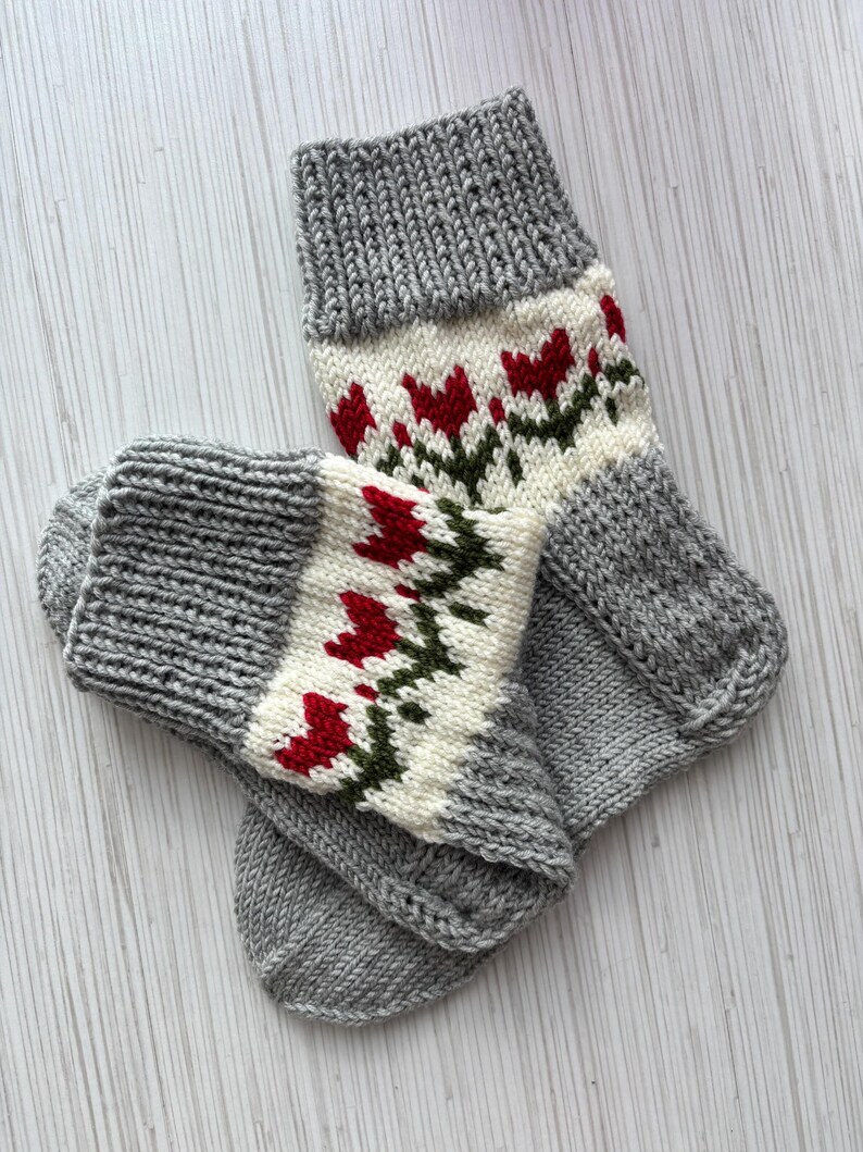 May include: A pair of gray knitted socks with a white and red floral pattern. The socks are folded together and have a ribbed texture.