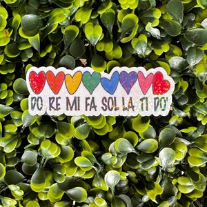 May include: A white sticker with a rainbow of glitter hearts and the text "DO RE MI FA SOL LA TI DO".
