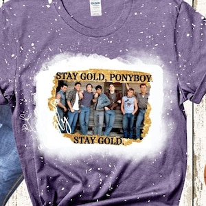 May include: Purple t-shirt with a white bleach design featuring a group of boys from the movie The Outsiders. The design includes the text "Stay Gold, Ponyboy" and "Stay Gold".