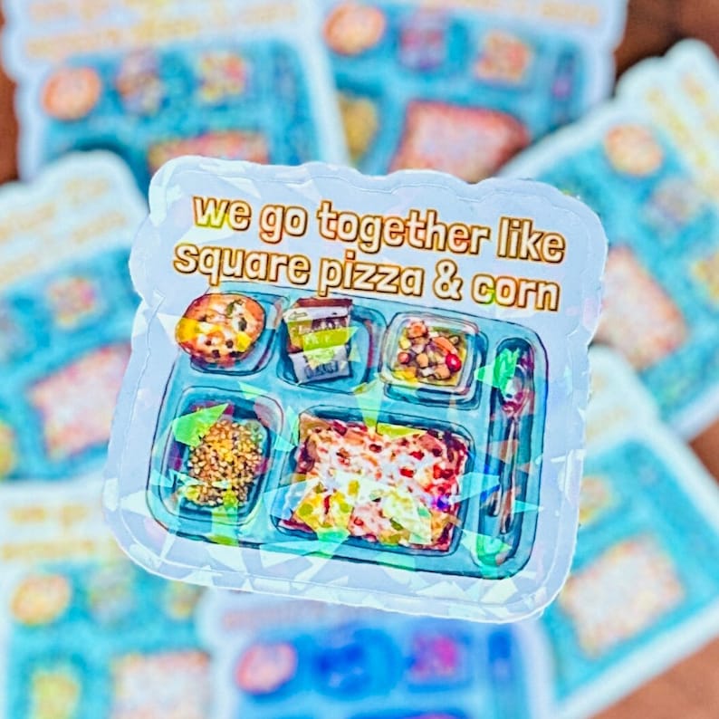May include: A holographic sticker with a blue and white lunch tray design. The tray has five compartments filled with different foods, including pizza, corn, and other items. The sticker has the text "we go together like square pizza & corn" in gold letters.