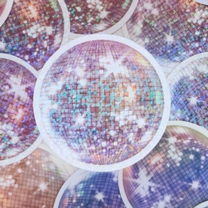 May include: A close-up of a group of iridescent disco balls with a white border. The disco balls are made of small, mirrored tiles that reflect light.