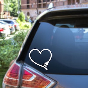 May include: White vinyl car decal featuring a heart shape with a stethoscope design. The decal is applied to the rear window of a gray car. The design is simple and clean, suitable for medical professionals or those in healthcare.