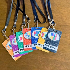 May include: A collection of colorful school hall passes with black lanyards. Each pass features a different design and text, including "Hall Pass," "Boy Rest," and "Girl Rest." The passes are attached to silver metal rings.