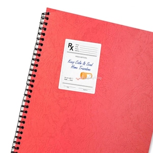 May include: A red spiral-bound notebook with a white prescription label affixed to the cover. The label reads "Keep Calm & Send Home Trazodone" with an illustration of a pill bottle and pills. The notebook's cover has a textured appearance.