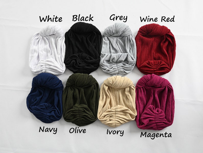 Puede incluir: Ocho diademas de turbante de diferentes colores, cada una con un nudo en la parte superior. Los colores son blanco, negro, gris, rojo vino, azul marino, oliva, marfil y magenta.