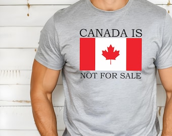 May include: A gray t-shirt with the text "CANADA IS NOT FOR SALE" printed on it. The text is in black and there is a red and white Canadian flag with a red maple leaf in the center.