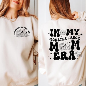 May include: A white sweatshirt with a black graphic on the front that says "Monster Truck Mom" and a black graphic on the back that says "In My Monster Truck Mom Era".