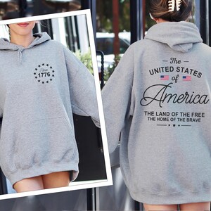 Pu&ograve; includere: Una felpa con cappuccio grigio m&eacute;lange con tasca frontale e cappuccio. La parte anteriore della felpa presenta un disegno circolare con la scritta "Since 1776". Il retro della felpa mostra la scritta "The United States of America".