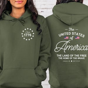 Pu&ograve; includere: Felpa con cappuccio verde oliva con tasca frontale e coulisse. La parte anteriore presenta un disegno bianco con il testo "Since 1776". Il retro mostra "The United States of America" con la bandiera americana e "The Land of the Free, The Home of the Brave".