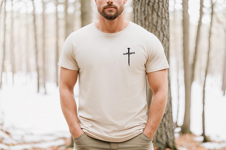 May include: A beige t-shirt with a black cross design featuring nails. The cross is centered on the chest of the shirt.