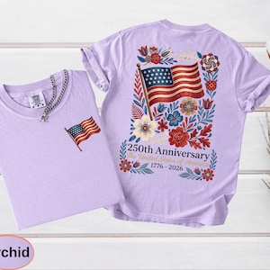 May include: Two orchid-colored t-shirts. One shirt has a small American flag embroidered on the chest. The other shirt features a large American flag design on the back, surrounded by flowers, with the text "250th Anniversary The United States of America 1776-2026."