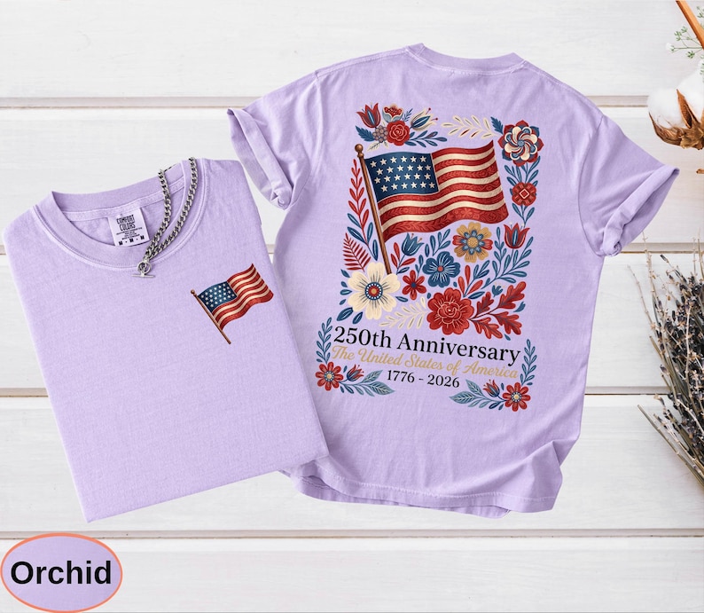 May include: Two orchid-colored t-shirts. One shirt has a small American flag embroidered on the chest. The other shirt features a large American flag design on the back, surrounded by flowers, with the text "250th Anniversary The United States of America 1776-2026."