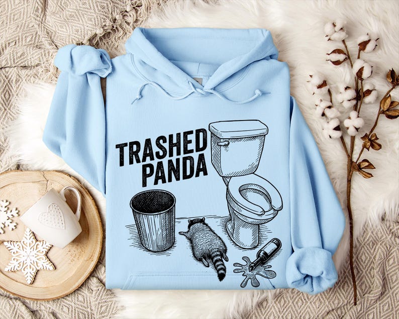 May include: Pale blue hoodie featuring the words "Trashed Panda" and a monochrome illustration of a toilet, bin, raccoon, and a spilled bottle. The design is in black and white.