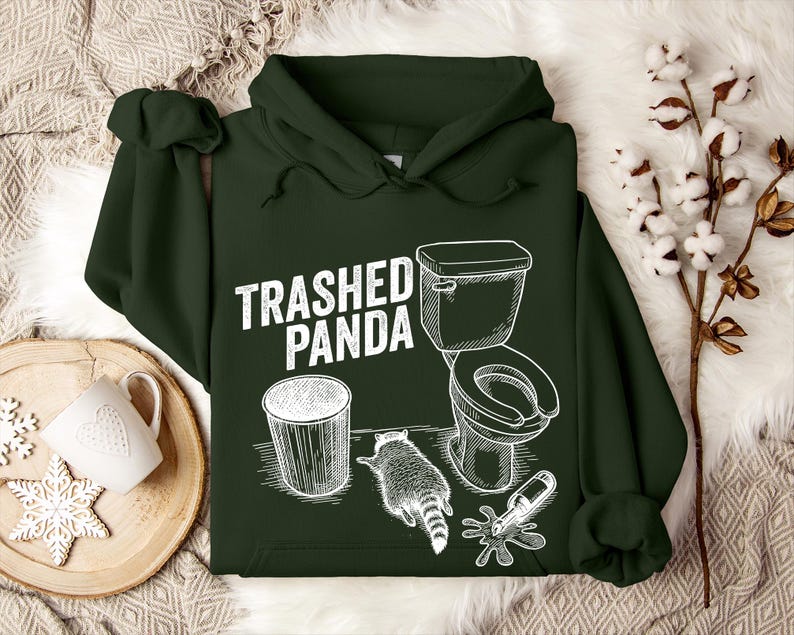 May include: Dark green hoodie featuring the text "Trashed Panda" and a white graphic of a toilet, bin, raccoon, and spilled bottle. The hoodie has a hood and a front pocket.