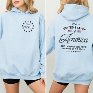 Pu&ograve; includere: Felpa con cappuccio azzurra con tasca frontale e cappuccio. La parte anteriore presenta un design circolare con il testo "Since 1776". Il retro della felpa con cappuccio mostra "The United States of America" con la bandiera americana e il testo "The Land of the Free, The Home of the Brave."