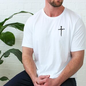 May include: A white t-shirt with a black cross with nails on it.