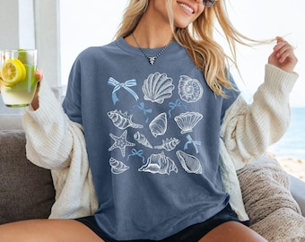 May include: A blue t-shirt with a white design of various seashells and starfish. The design includes blue bows.