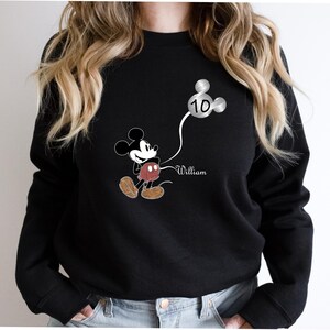 Puede incluir: Sudadera negra con un gr&aacute;fico de Mickey Mouse sosteniendo un globo plateado que dice "10" y el nombre "William" impreso debajo.