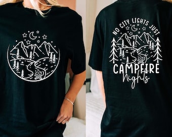 May include: Black t-shirt with a white graphic of a mountain scene, river, and campfire. The back of the shirt features the text "No City Lights Just Campfire Nights" in white. A casual, comfortable tee.