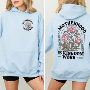 May include: Light blue hoodie with the text "MOTHERHOOD IS KINGDOM WORK" and a floral design on the front and back. The back design includes additional text and the Bible verse Proverbs 31:25-27.