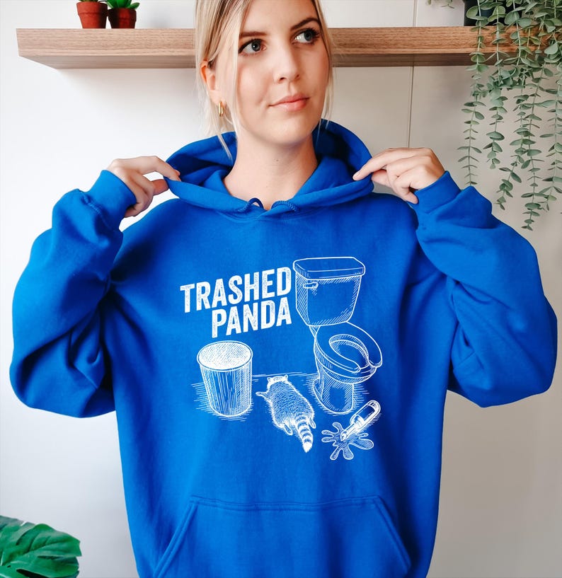 May include: A bright blue hoodie with a white graphic that says "Trashed Panda." The graphic includes a bin, a toilet, a raccoon, and a spilled bottle. The hoodie has a hood and a front pocket.