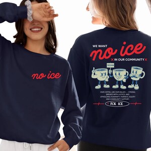 May include: Navy blue sweatshirt with the words "no ice" in red script on the front. The back features the phrase "We want no ice in our community" with cartoon coffee cups and the text "FCK ICE".