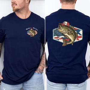 May include: Navy blue t-shirt featuring a graphic of a largemouth bass wearing a red and white hat, set against a stylized American flag. The shirt also has the text "Hooked on Freedom" on the front.