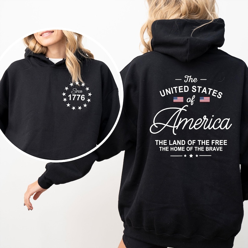 Pu&ograve; includere: Felpa con cappuccio nera con testo e grafica bianchi. La parte anteriore presenta un design circolare con "Since 1776". Il retro mostra "The United States of America" con la bandiera americana e le frasi "The Land of the Free" e "The Home of the Brave".