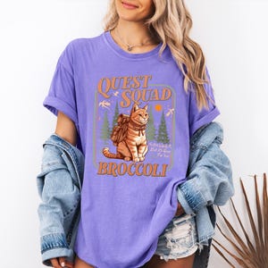 May include: Purple t-shirt with a graphic of a cat wearing a backpack and the text "Quest Squad Broccoli".
