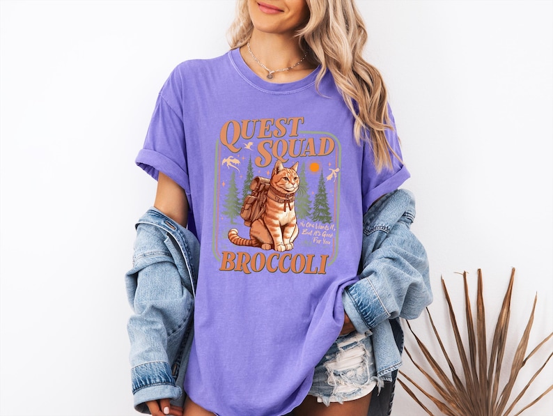 May include: Purple t-shirt with a graphic of a cat wearing a backpack and the text "Quest Squad Broccoli".