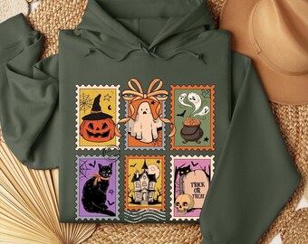 May include: Dark green Halloween-themed hoodie featuring a collage of vintage-style postage stamps. The stamps depict a jack-o'-lantern, ghost, cauldron, black cat, haunted house, and tombstone with the text "Trick or Treat".