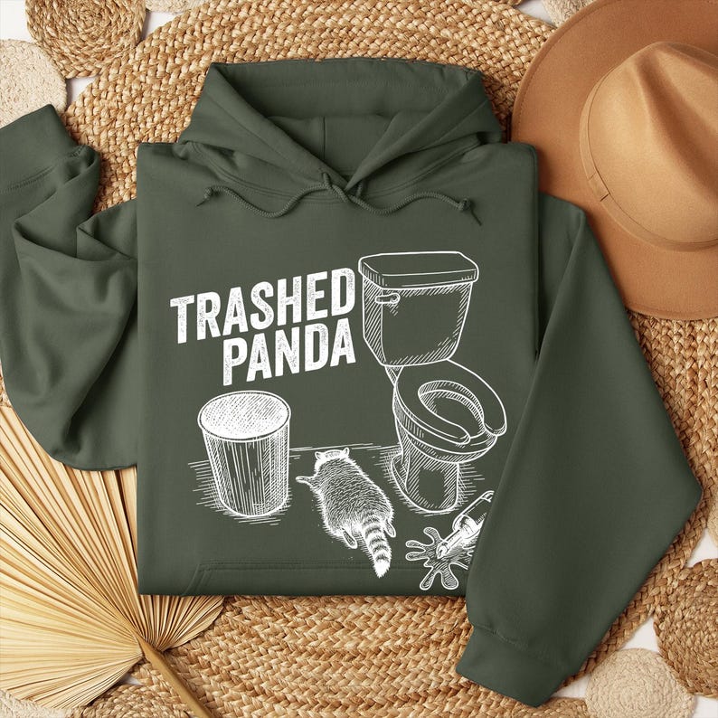 May include: Dark green hoodie featuring the text "Trashed Panda" and a white graphic of a raccoon, toilet, and bin. The design contrasts with the hoodie's colour. The hoodie includes a hood and drawstrings.