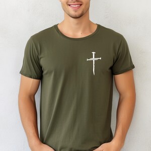 May include: A green t-shirt with a white cross design featuring nails. The cross is a simple design with a vertical line and a horizontal line, and the nails are represented by small circles.