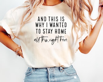 May include: Cream-colored t-shirt with the text "AND THIS IS WHY I WANTED TO STAY HOME all this, right here." in black. The shirt is paired with blue denim jeans.