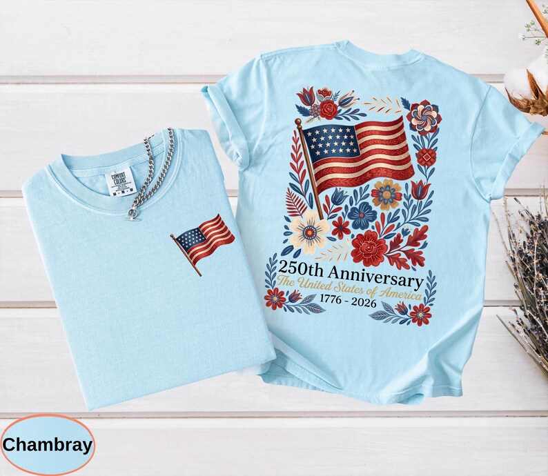 May include: Two light blue t-shirts. One has a small American flag embroidered on the chest. The other has a large American flag design on the back, surrounded by flowers and the text "250th Anniversary The United States of America 1776-2026."