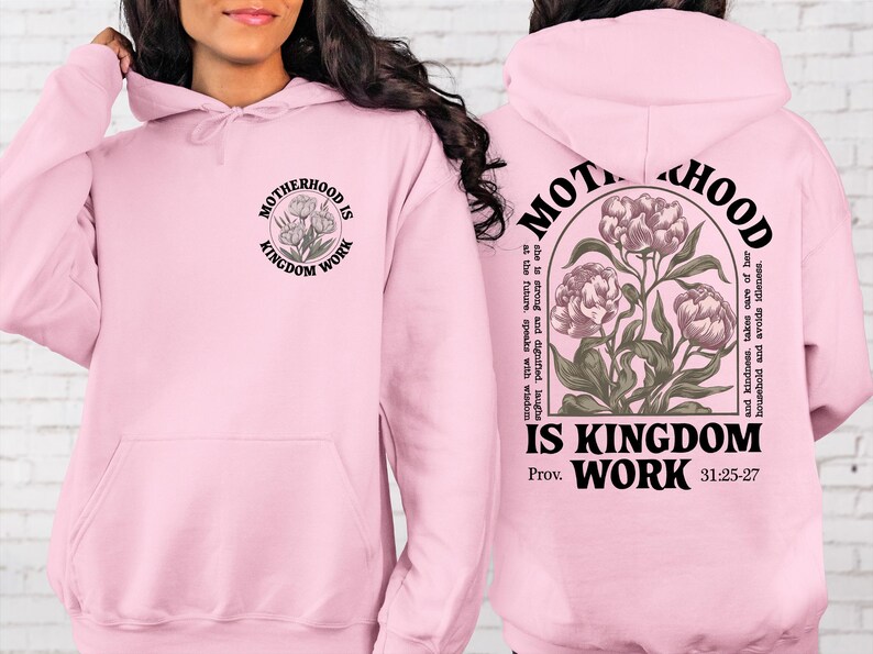 May include: Light pink hoodie with the text "MOTHERHOOD IS KINGDOM WORK" and a floral design. The back of the hoodie has the same text and design, along with a Bible verse reference. A comfortable and stylish sweatshirt.