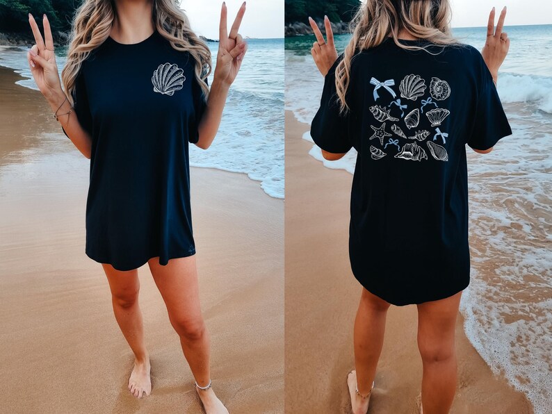 Puede incluir: Camiseta negra con un dise&ntilde;o de concha blanca en la parte delantera y una colecci&oacute;n de conchas en la parte trasera. La camiseta se usa en una playa con el oc&eacute;ano de fondo.