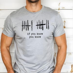 May include: A light gray t-shirt with the phrase "if you know you know" printed in black. The design includes two sets of tally marks, each with a line through them. The shirt is made of a soft material.