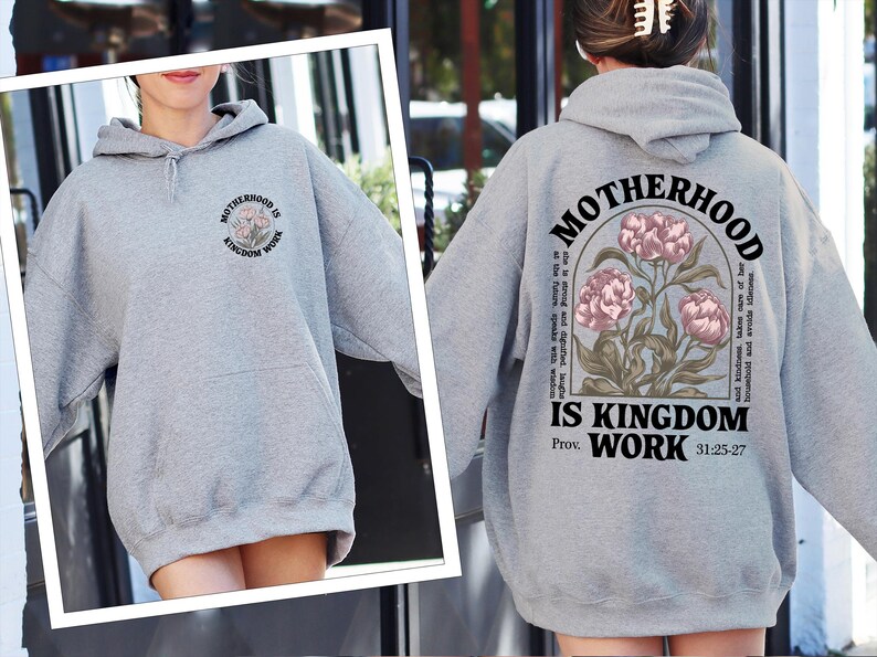 May include: A heather gray hoodie with the text "MOTHERHOOD IS KINGDOM WORK" and a floral design. The back of the hoodie features the same text and design, along with a Bible verse. A comfortable, casual sweatshirt.