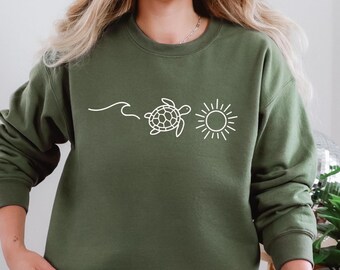 May include: Olive green sweatshirt featuring a white graphic of a wave, a sea turtle, and a sun. The design is simple and minimalist. The sweatshirt is a crew neck style.