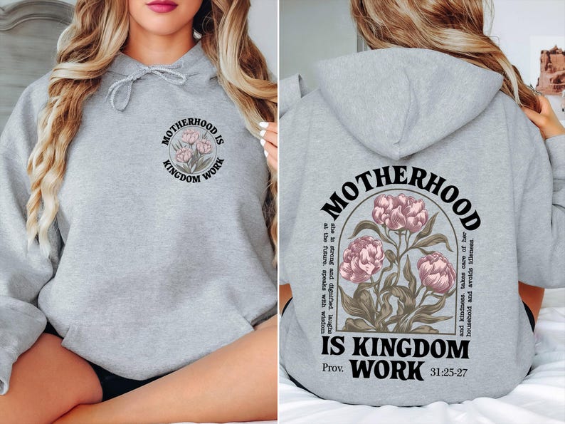 May include: A light gray hoodie with the text "MOTHERHOOD IS KINGDOM WORK" and a floral design. The back of the hoodie features the same text and design, along with additional text. The hoodie has a drawstring hood.