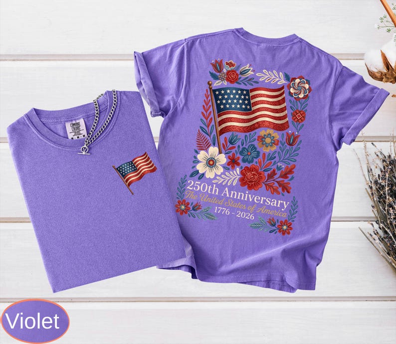 May include: Two violet t-shirts. One has a small American flag embroidered on the chest. The other has a large American flag design on the back, surrounded by flowers, with the text "250th Anniversary The United States of America 1776-2026".
