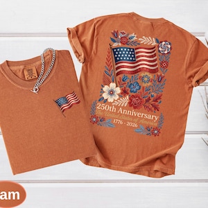 May include: Two yam-colored t-shirts. One has a small embroidered American flag on the chest. The other features a large American flag design on the back, surrounded by flowers, with the text "250th Anniversary The United States of America 1776-2026."